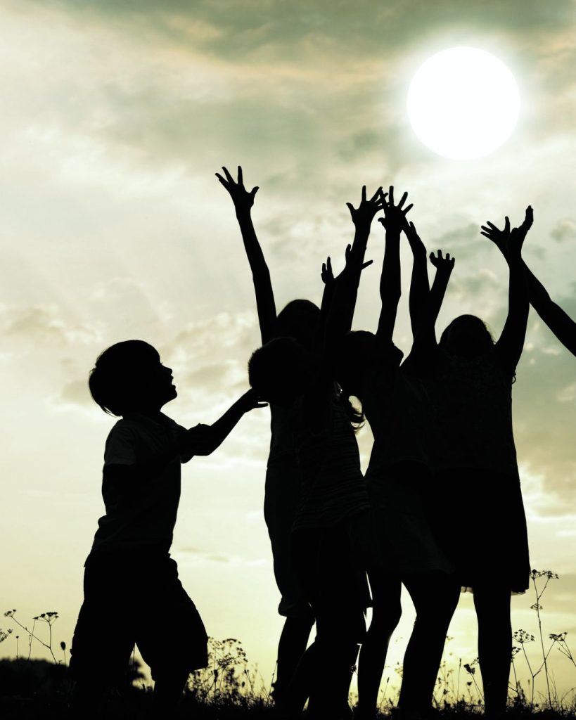 Silhouettes of children playing with their arms raised against a bright sky, symolising joy, freedom, and emotional growth.