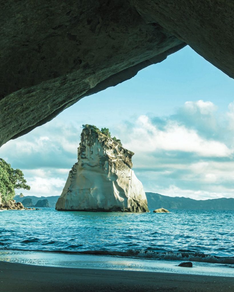 Large rock formation rising from the sea, framed by an overhanging cliff.