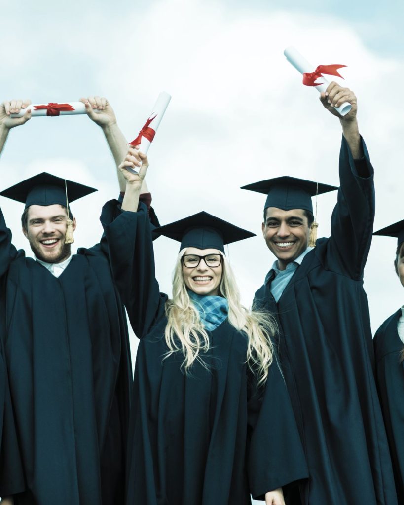 Group of smiling graduates in caps and gowns, raising their arms in celebration.