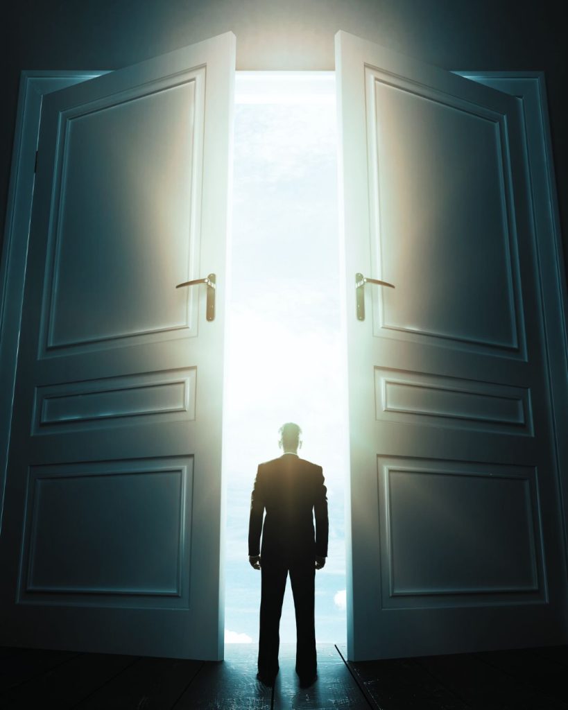 Silhouette of a person standing in a bright doorway between two large open doors, symbolising new career opportunities and pathways.
