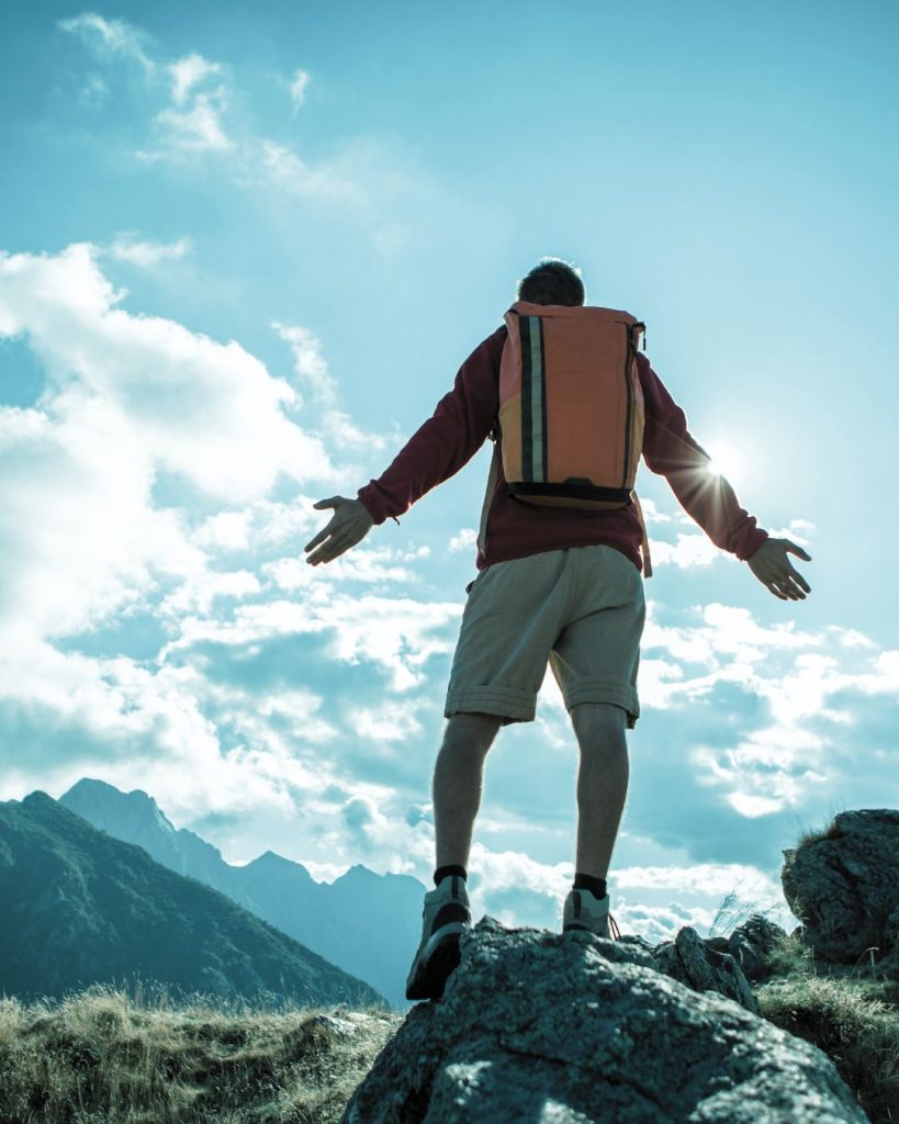Man standing on a mountain with a backpack, arms open towards the sky.