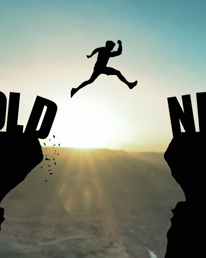 Silhouette of a person leaping from the word "Old" to the word "New" at sunrise.