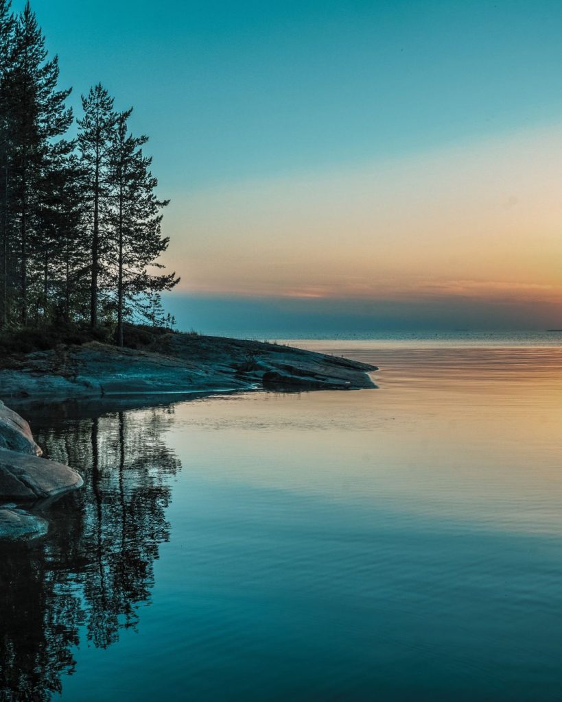 Calm blue and orange sky reflecting on a peaceful lake with trees, creating a soothing and grounding scene.