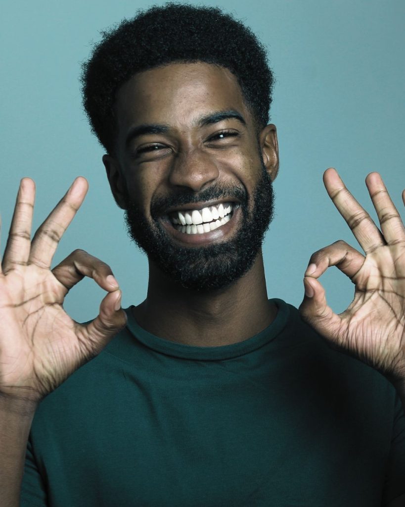 Smiling man making two "ok" hand gestures, expressing positivity and satisfaction.