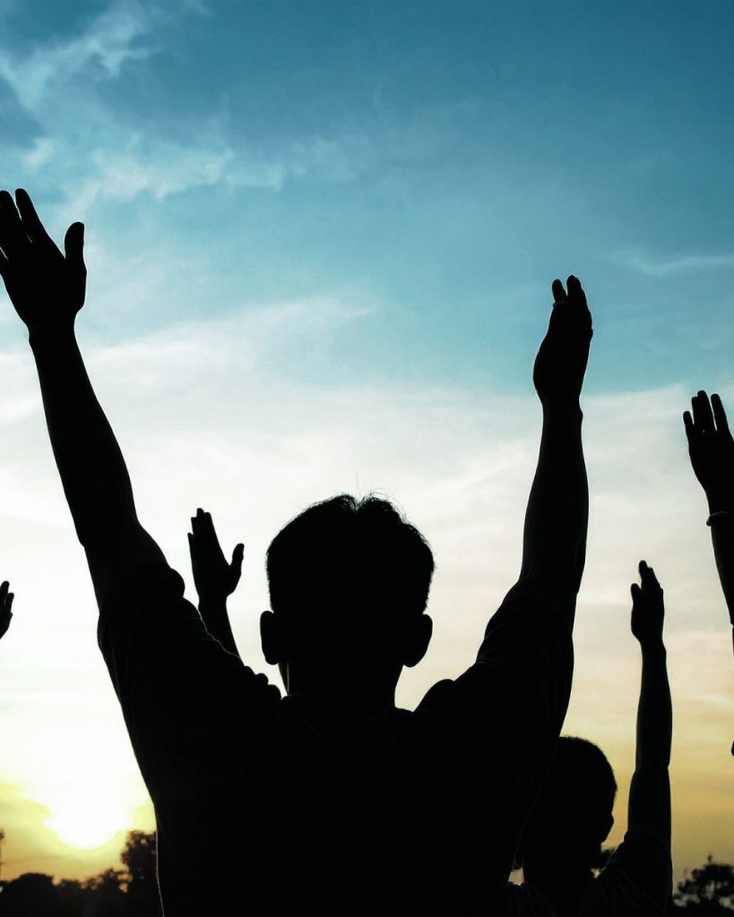 Silhouette of young people with their arms raised at sunset.